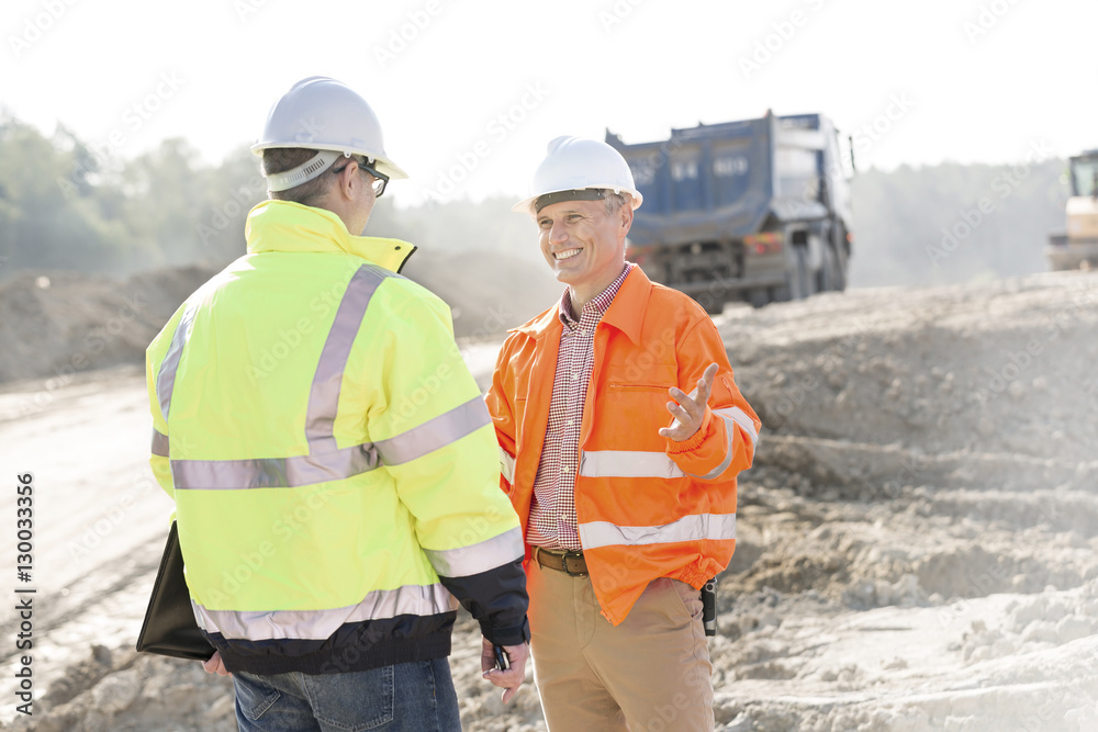 Happy engineer talking to colleague at construction site on sunny day Happy engineer talking to colleague at construction site on sunny day