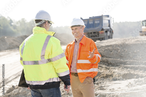 Happy engineer talking to colleague at construction site on sunny day