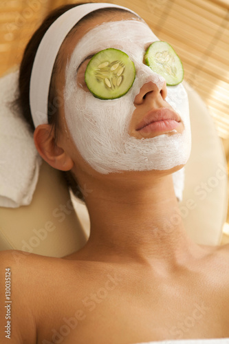 Young woman lying down on massage table with cucumbers on eyes