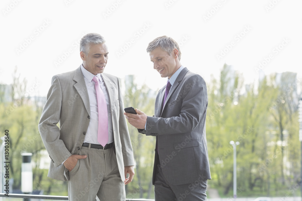 Businessmen using cell phone together outdoors Businessmen using cell phone together outdoors