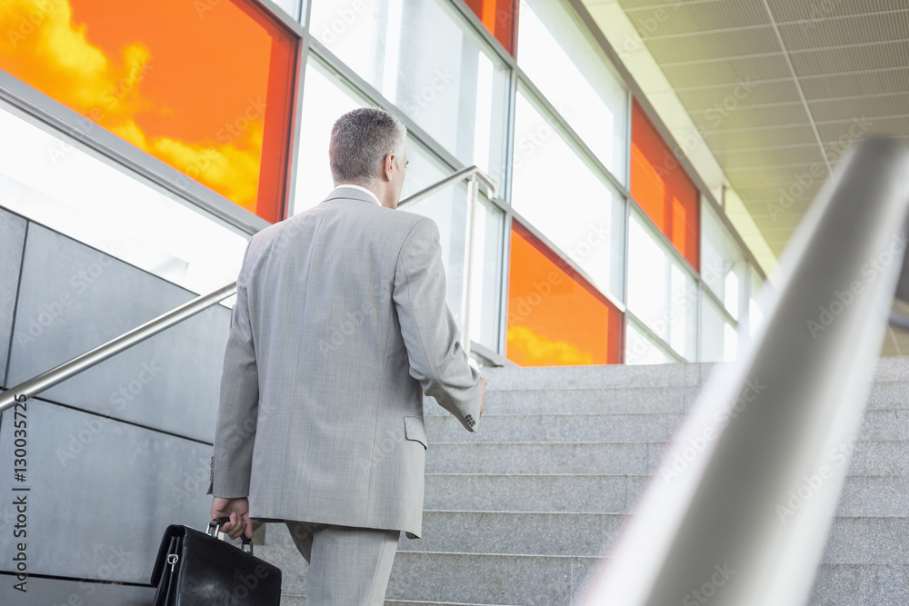 Fototapeta premium Rear view of middle aged businessman walking up stairs in railroad station