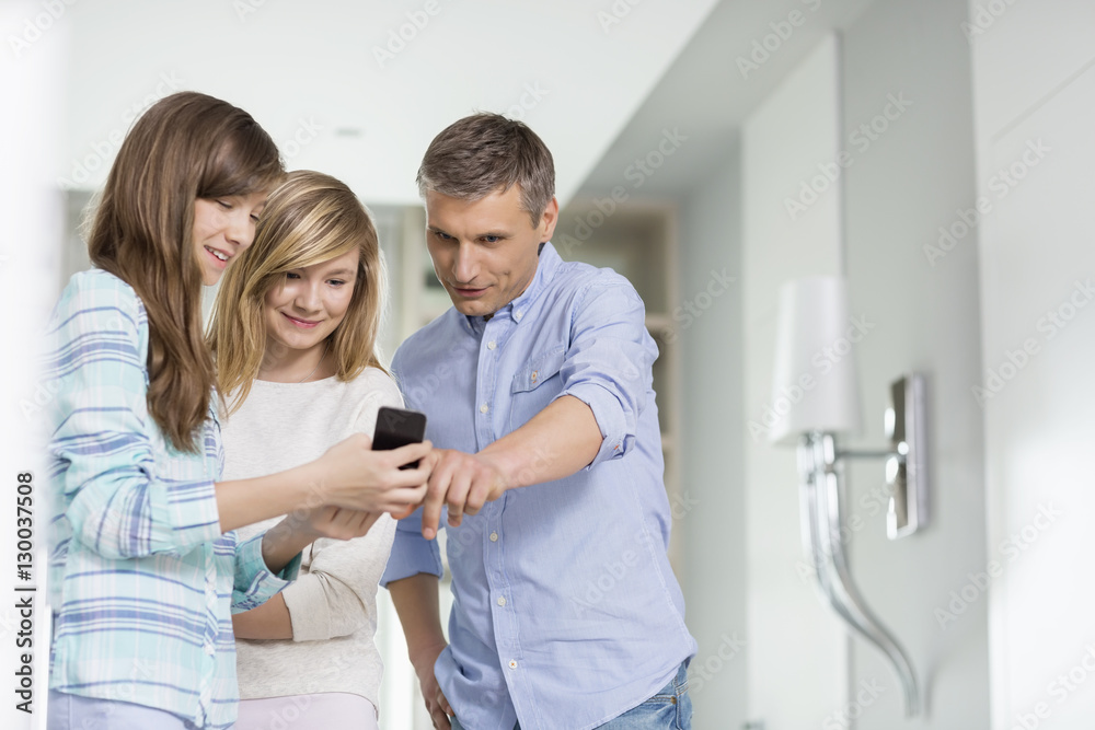 Obraz premium Middle-aged man with daughters using smart phone at home