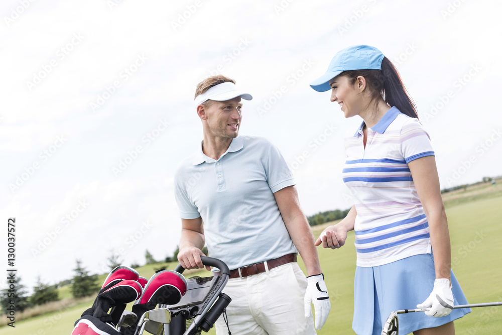 Naklejka premium Happy man and woman conversing at golf course against clear sky