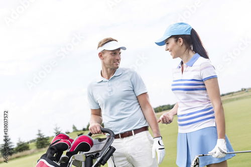 Happy man and woman conversing at golf course against clear sky © moodboard