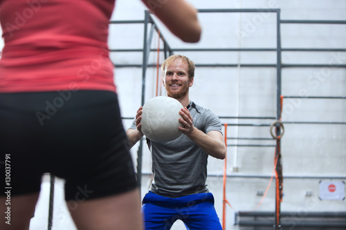 Happy man throwing medicine ball towards woman in crossfit gym