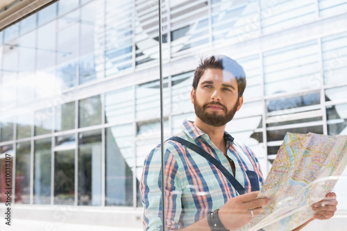 Thoughtful man looking away while holding road map against glass wall