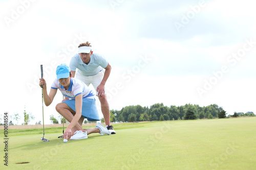 Man with woman aiming ball on golf course against sky