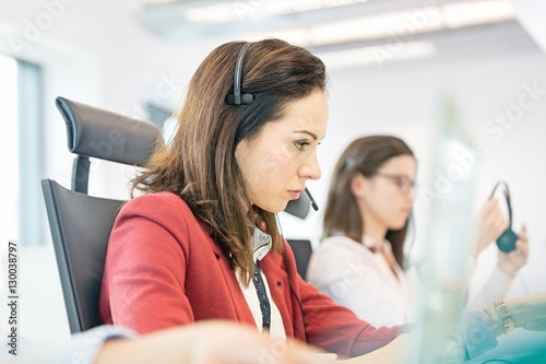 Young businesswoman using headset with female colleague in background at office