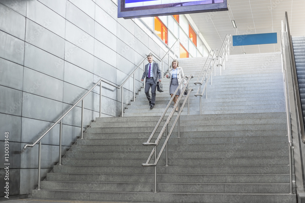 Full length of businessman and businesswoman walk down stairs at railway station