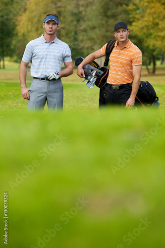 Young men standing on golf course carrying bags
