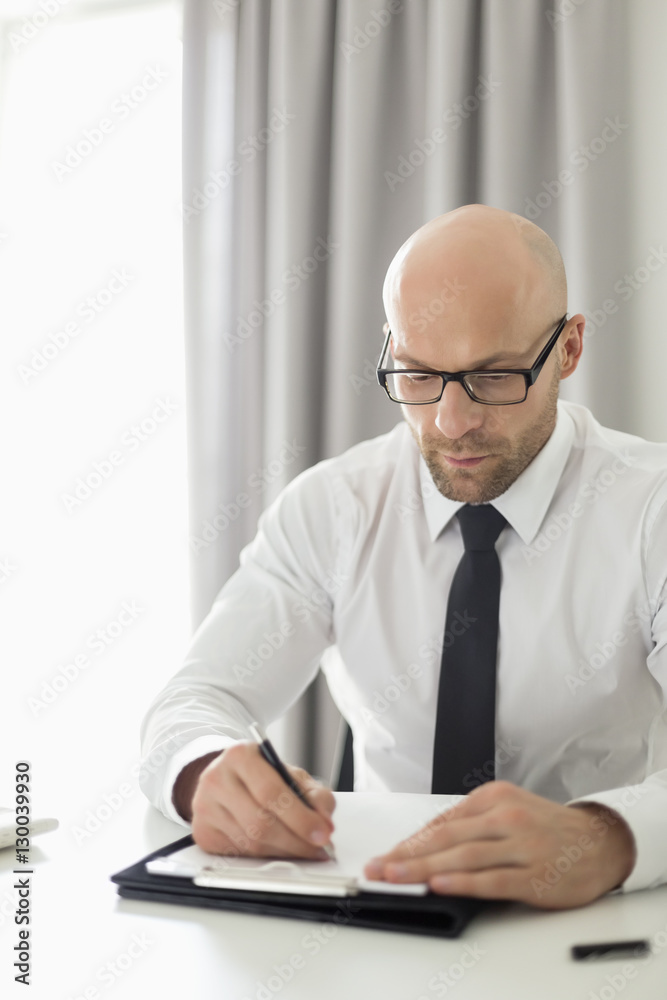 Mid adult businessman writing on clipboard in home office Mid adult businessman writing on clipboard in home office