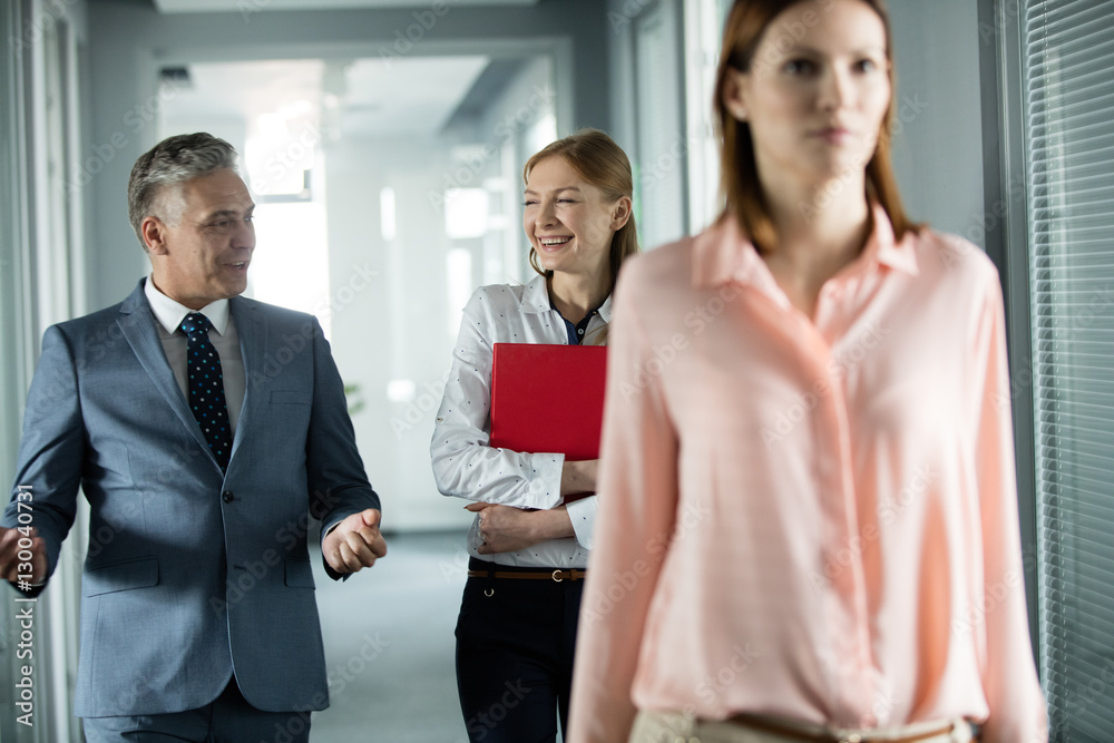 Businessman and businesswoman talking while walking in corridor with female colleague in foreground at office Businessman and businesswoman talking while walking in corridor with female colleague in foreground at office