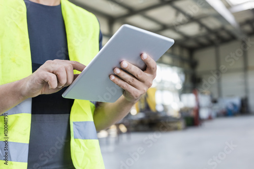 Midsection of manual worker using digital tablet in metal industry