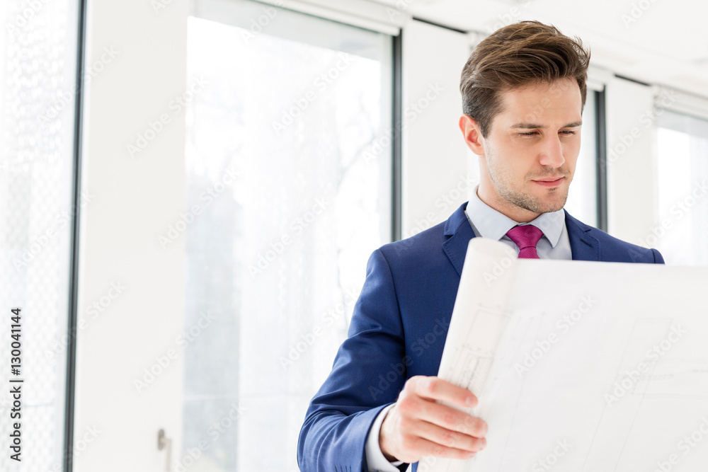Confident young businessman reading blueprint in new office Confident young businessman reading blueprint in new office