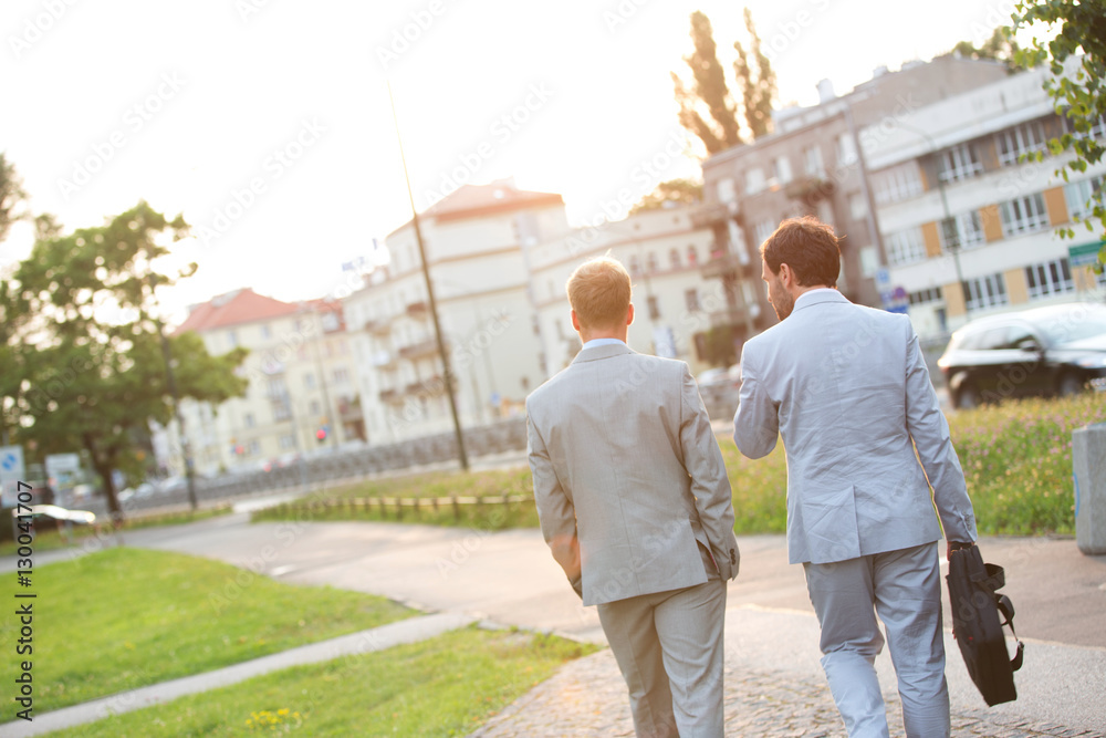 Rear view of businessmen walking at park on sunny day Rear view of businessmen walking at park on sunny day