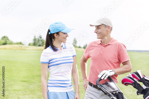 Happy male and female golfers communicating against clear sky