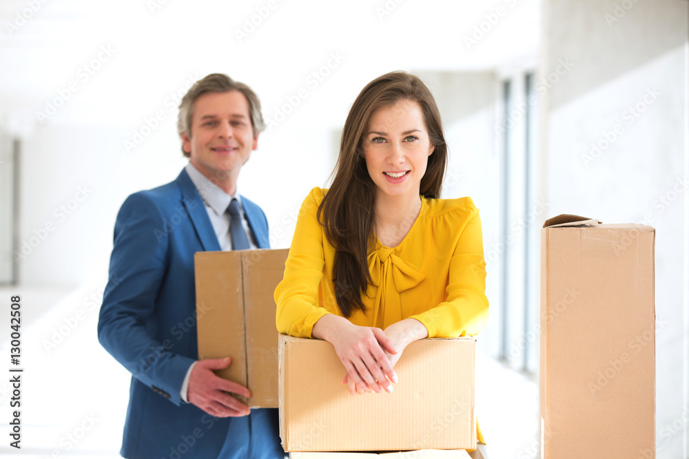 Portrait of confident businesswoman and male colleague with cardboard boxes in new office