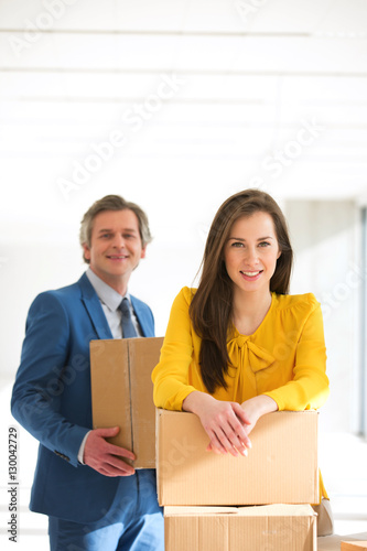 Portrait of businesswoman and male colleague with cardboard boxes in new office © moodboard