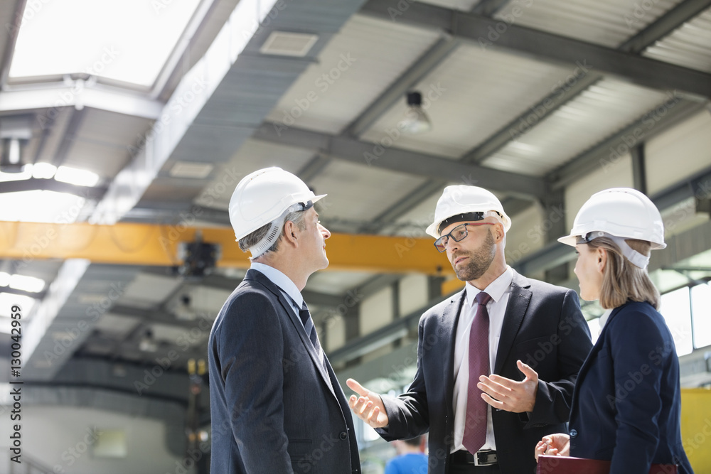 Business people wearing hardhats having discussion in metal industry Business people wearing hardhats having discussion in metal industry
