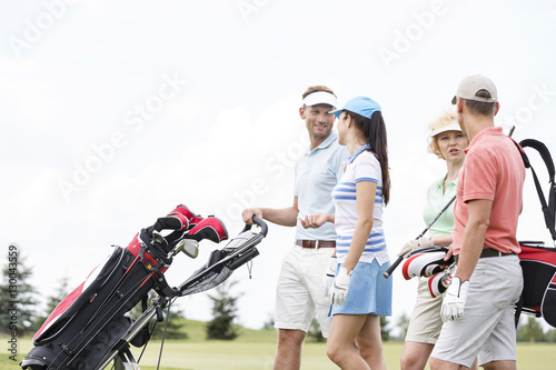 Friends communicating while walking at golf course against clear sky