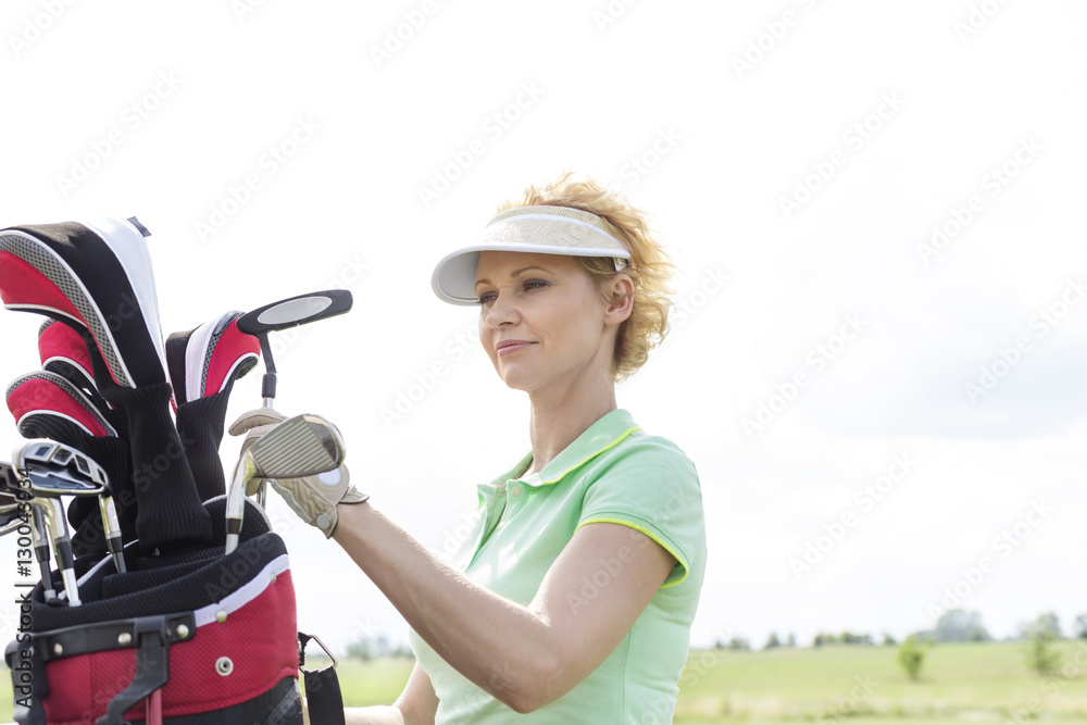 Female golfer with golf club bag against clear sky