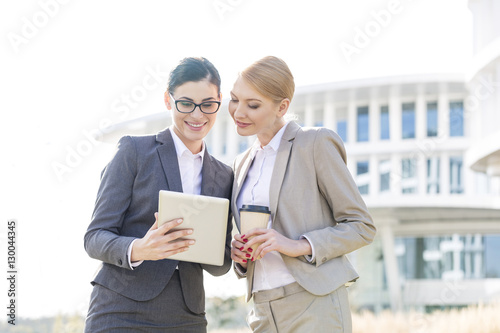 Happy businesswomen using tablet PC outside office building