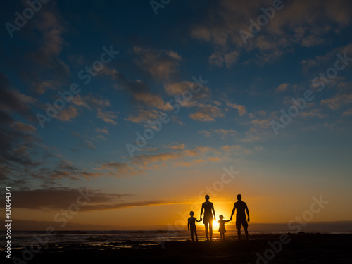Family at sunset by the ocean. People hold hands and look at the