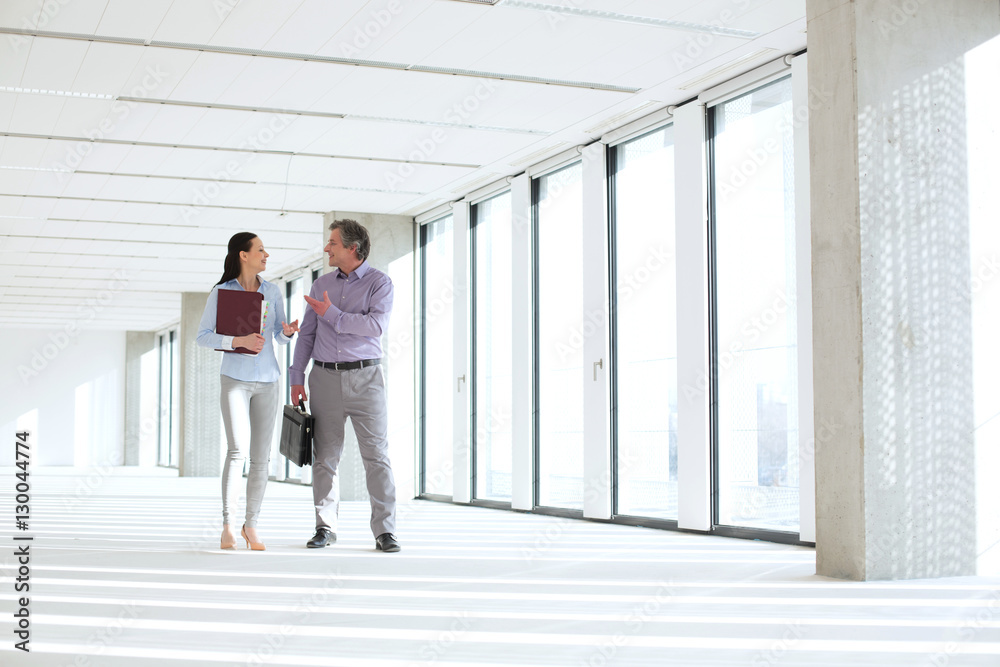 Businessman and businesswoman talking while walking in empty office