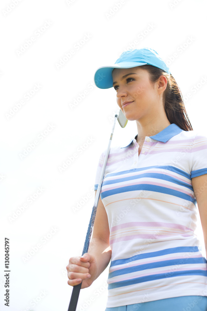 Confident woman looking away while holding golf club against clear sky Confident woman looking away while holding golf club against clear sky