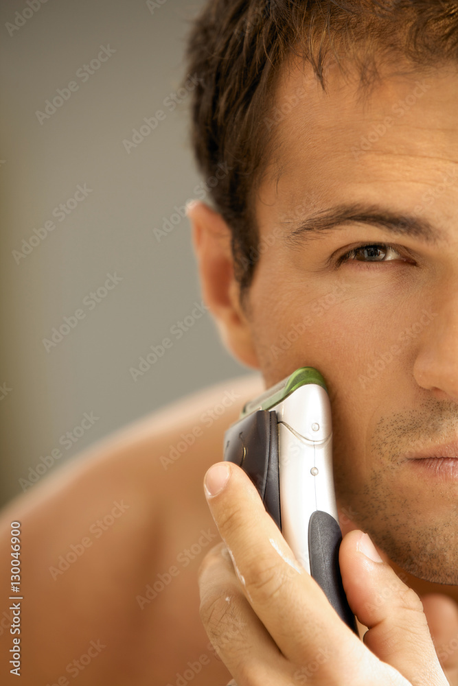 Reflection of young man in mirror shaving with electric shaver Reflection of young man in mirror shaving with electric shaver