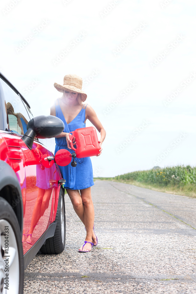 Full length of young woman refueling car on country road Full length of young woman refueling car on country road