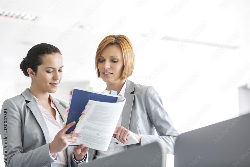 Young businesswomen discussing over book in office Young businesswomen discussing over book in office