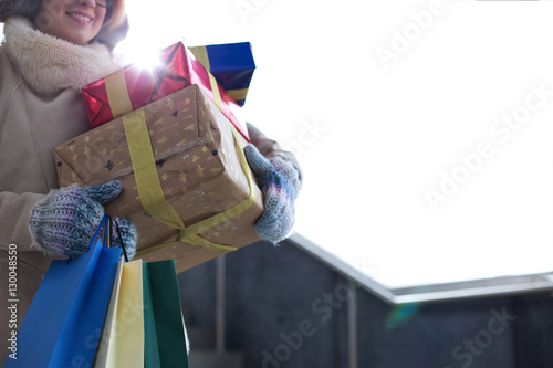 Midsection of woman with stacked gifts and shopping standing by window during winter