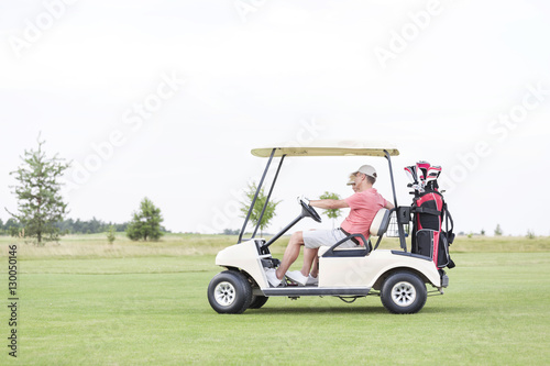 Side view of couple sitting in golf cart against clear sky