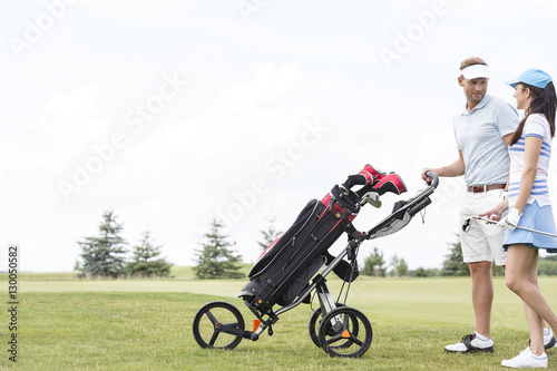 Friends with equipment talking while walking at golf course against clear sky