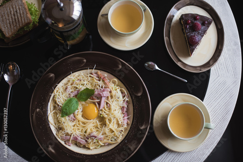 Classic Pasta carbonara  with bacon and egg yolk, egg and Parmesan with two cups of tea and desserts. photo