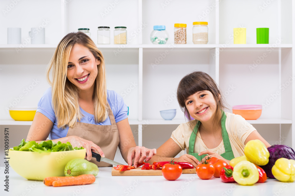 Happy mother and her daughter enjoy making healthy meal together at their home. 
