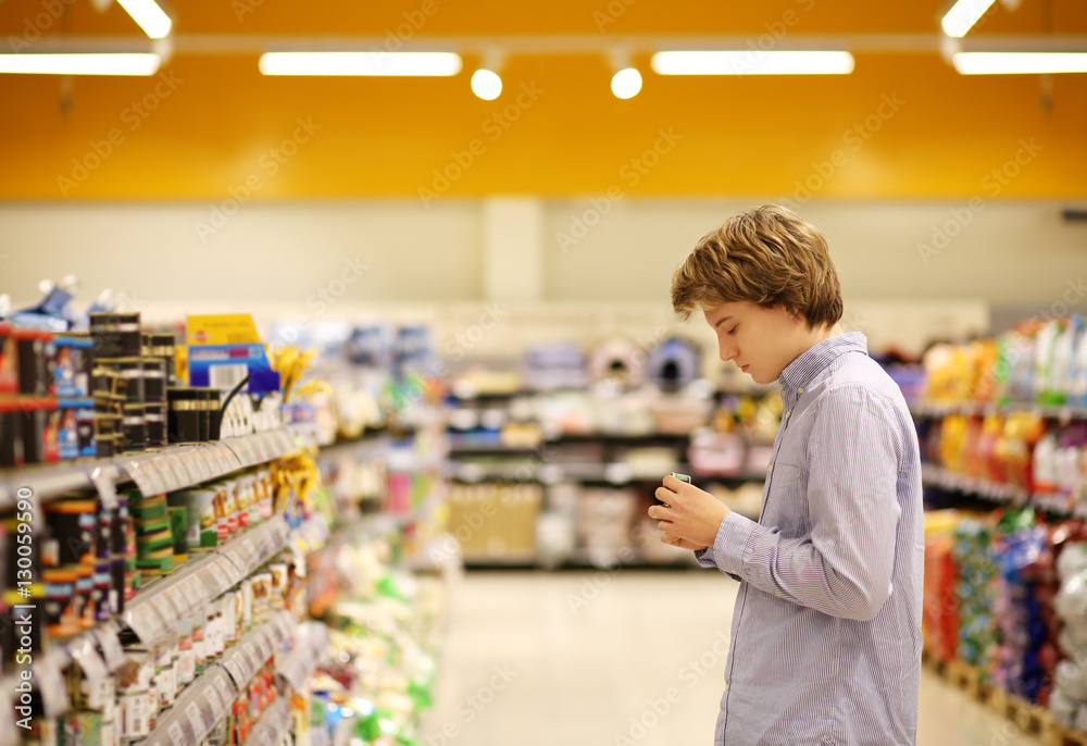 Man shopping in supermarket reading product information. Checking list.
