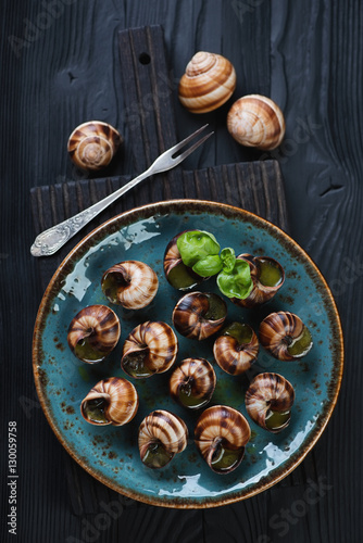 Baked snails with garlic butter on a black wooden background
