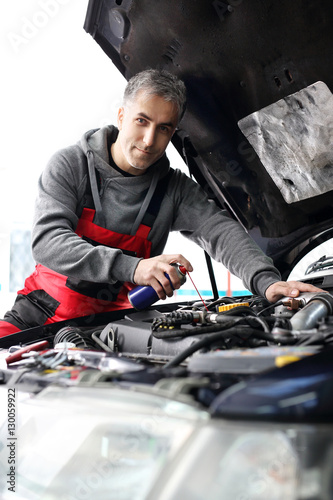 Mechanik samochodowy czyści i smaruje śruby pod maską samochodu © Robert Przybysz