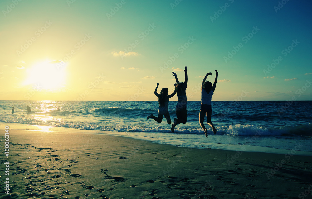 Fototapeta premium Three girlfriends jumping on the beach at sunset