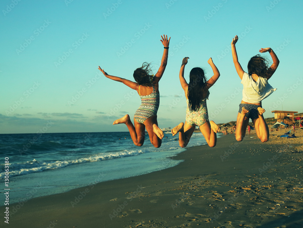 Three girlfriends jumping on the beach at sunset