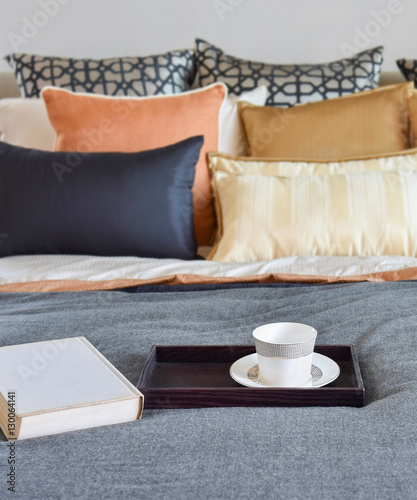 modern bedroom interior with teacup on decorative wooden tray and white book on the bed