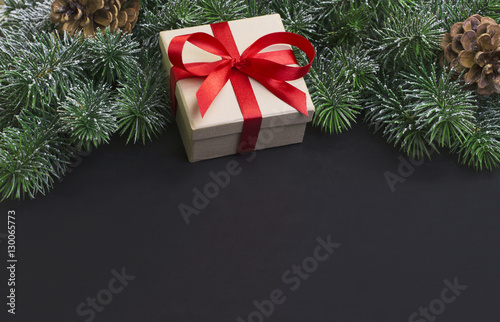Gift and snow covered branches of Christmas tree on a black background.