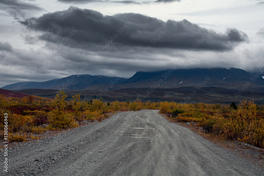 The road to the mountains and a dark cloud over the mountains. Polar Urals. Russia.