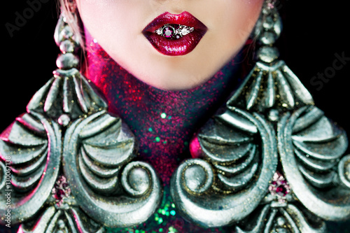 Sick of glamour. Girl with bright makeup and huge earrings. Precious stones or jewelry in mouth. Cncept