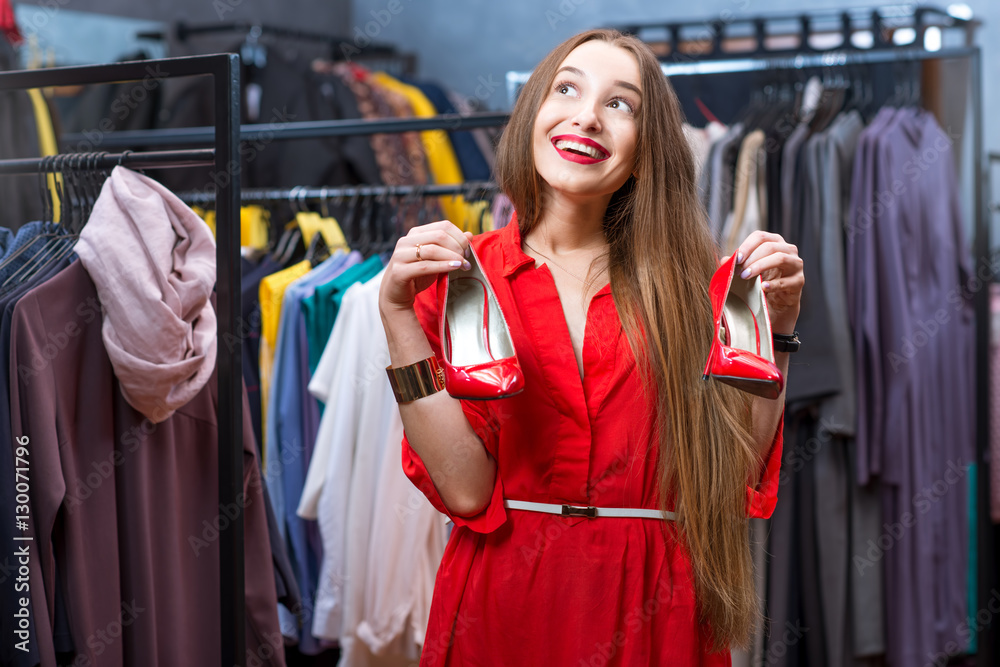 Young woman in the red dress choosing shoes in the luxury clothing store