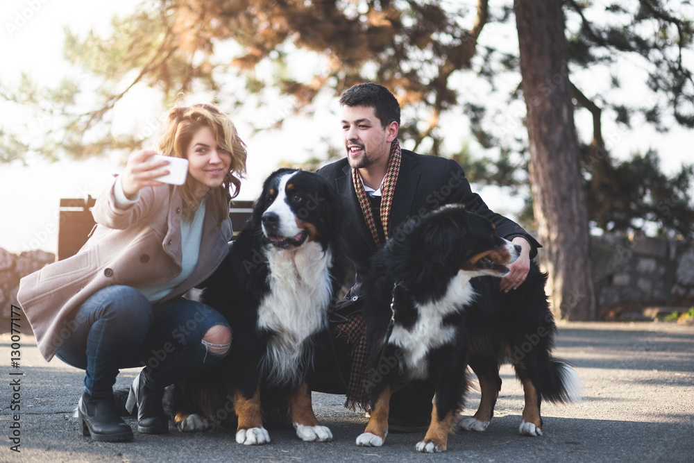 Young couple taking selfie photo with their adorable Bernese Mountain dogs. Young couple taking selfie photo with their adorable Bernese Mountain dogs.