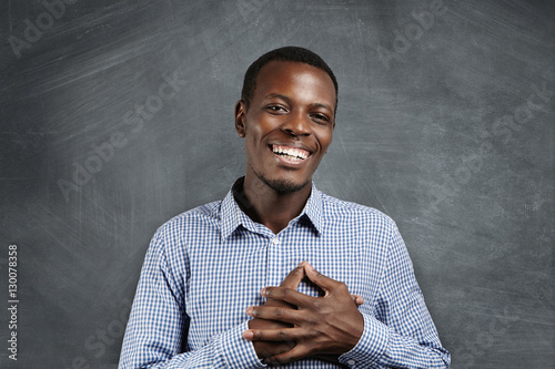 Canvas Print Touched and grateful African man smiling happily, holding hands on his chest to express his gratitude and thankfulness