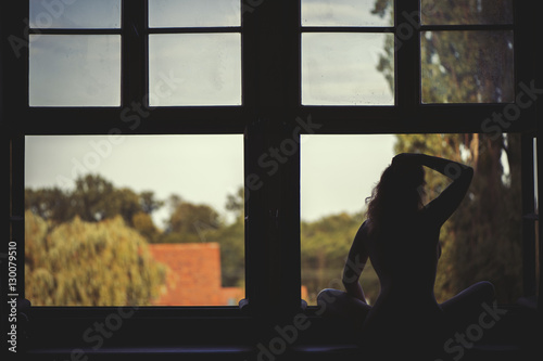 Beautiful naked woman sitting on a window at sunset 